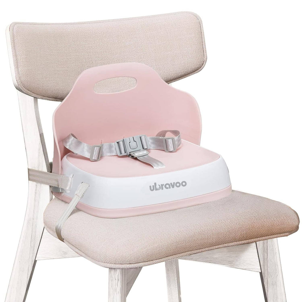 Pink booster seat with gray straps on a light wood chair with fabric backrest