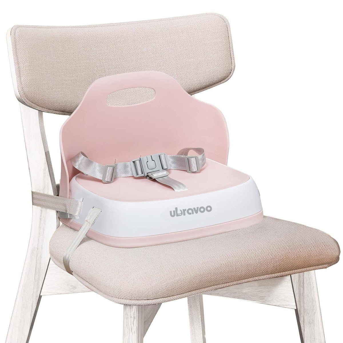 Pink booster seat with gray straps on a light wood chair with fabric backrest