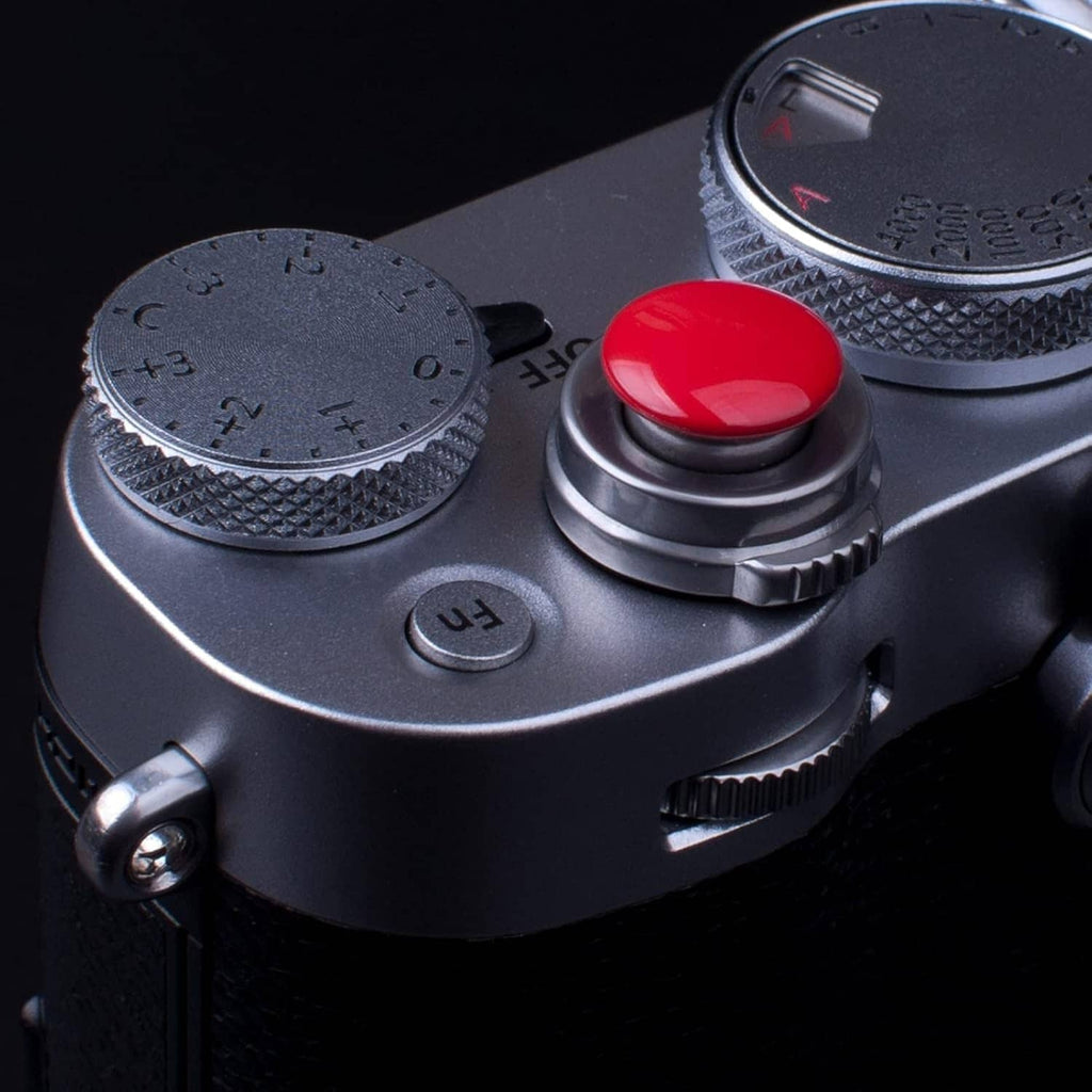Red shutter release button on camera top with textured dial and labeled mode ring.