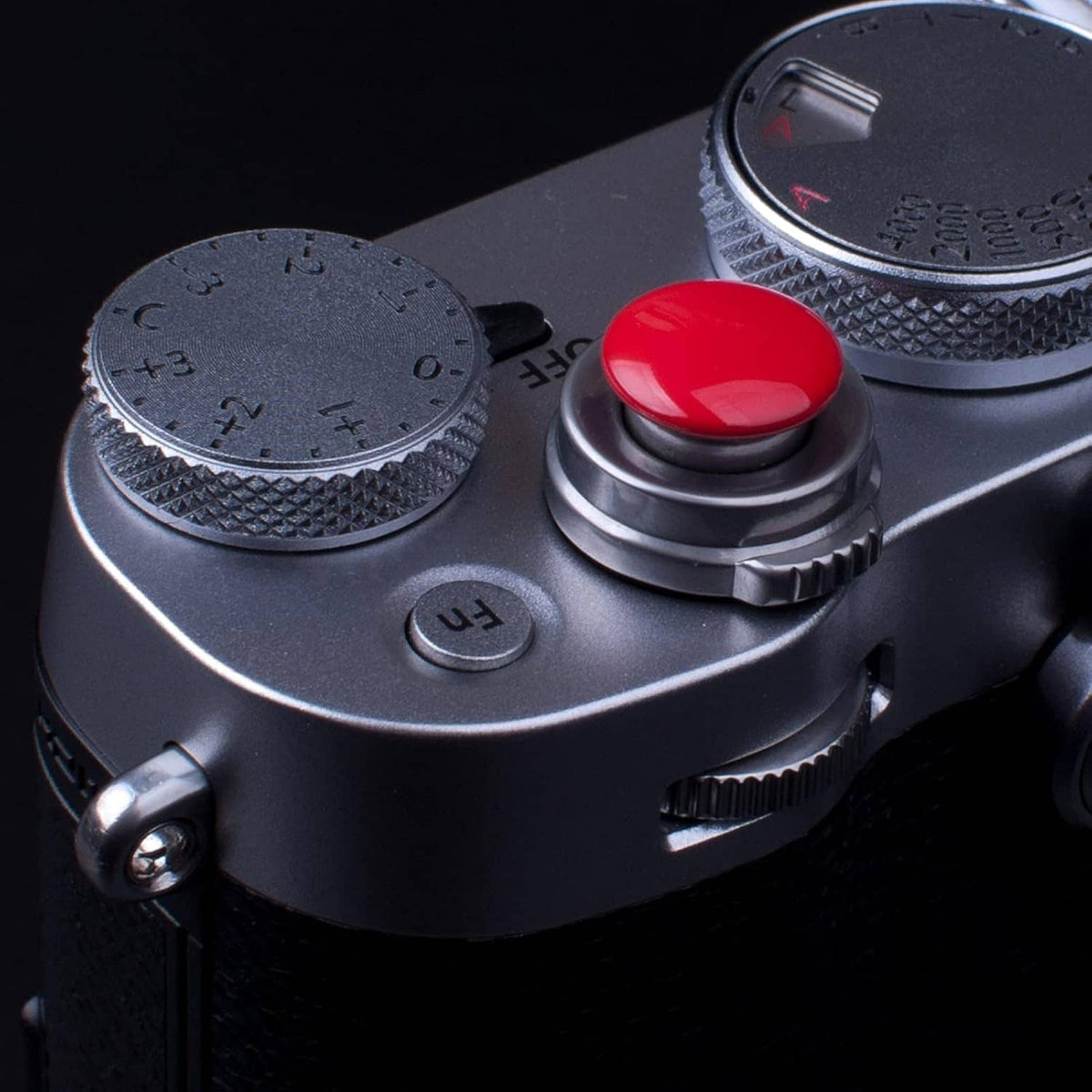Red shutter release button on camera top with textured dial and labeled mode ring.