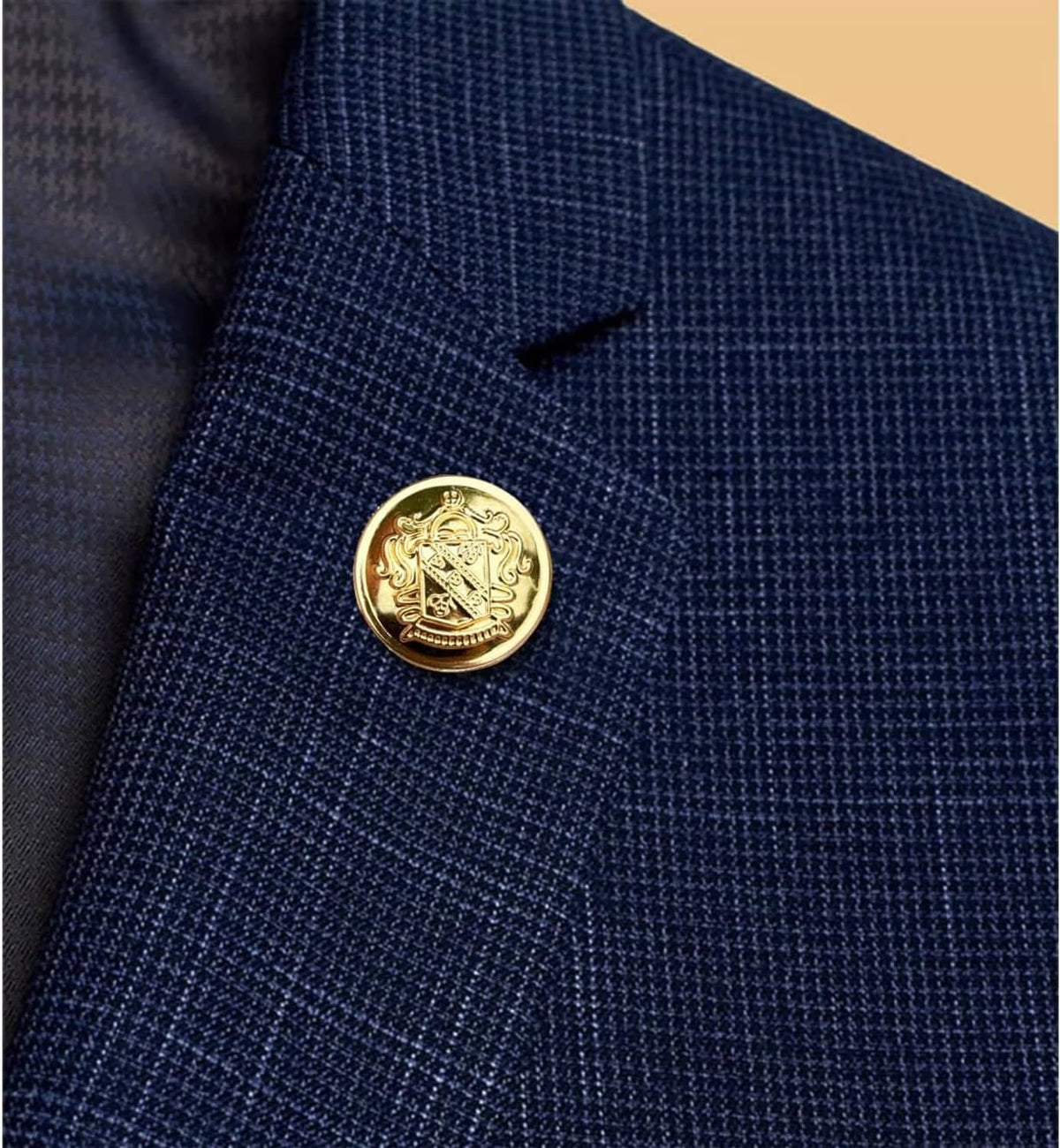 Round gold blazer button with engraved crest, on navy textured jacket fabric