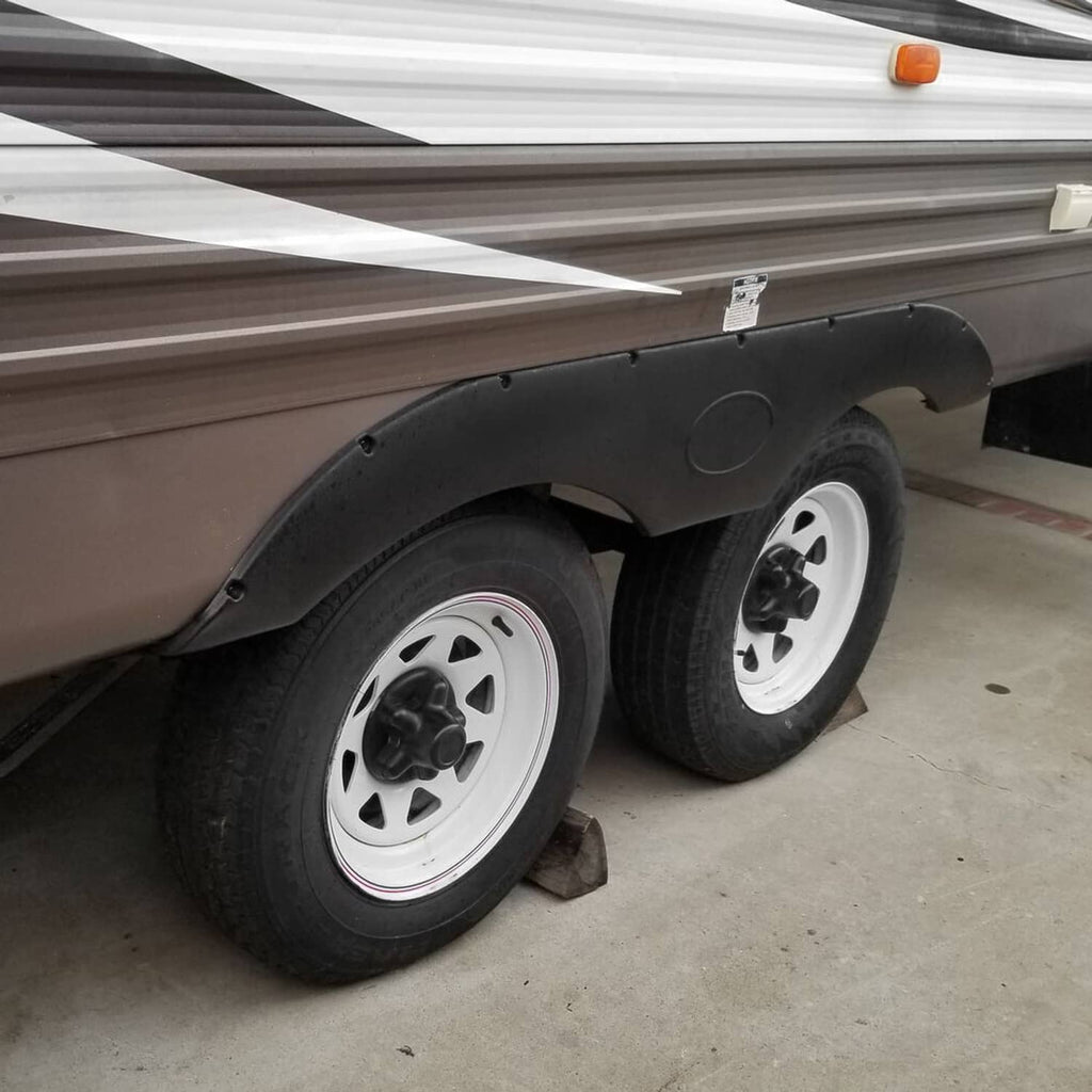 Black RV trailer fender skirt installed over wheel, curved molded cover with oval emblem