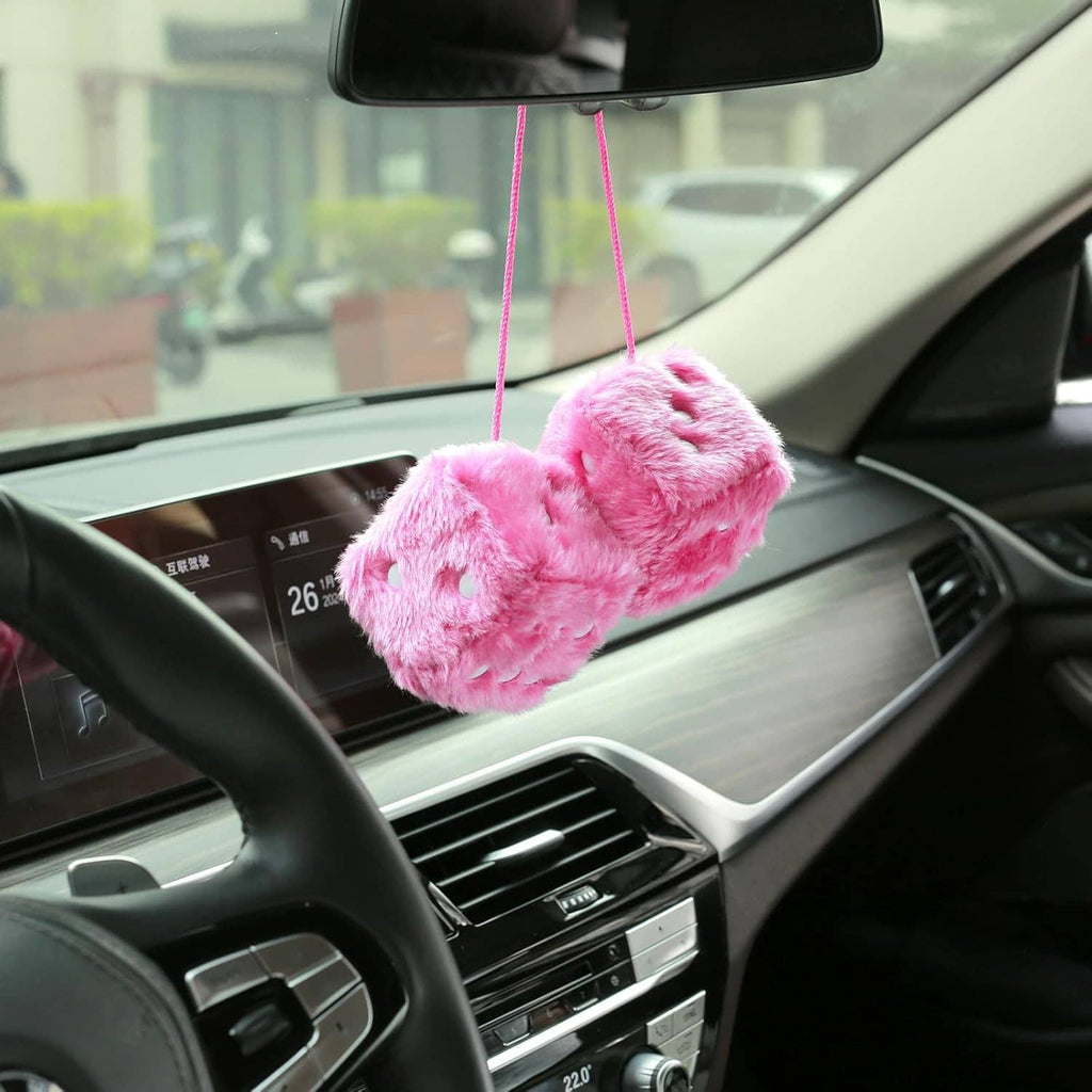 Pink fuzzy dice hanging from the rearview mirror with white pips and pink cords