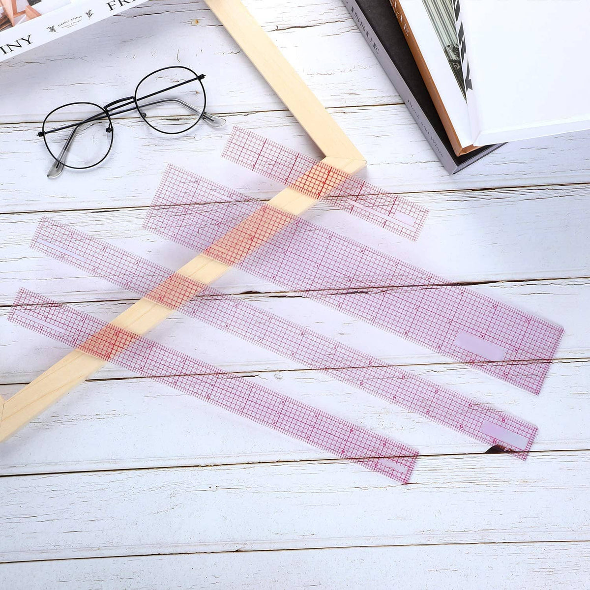 Clear plastic grid rulers with red markings arranged on a work surface for measuring