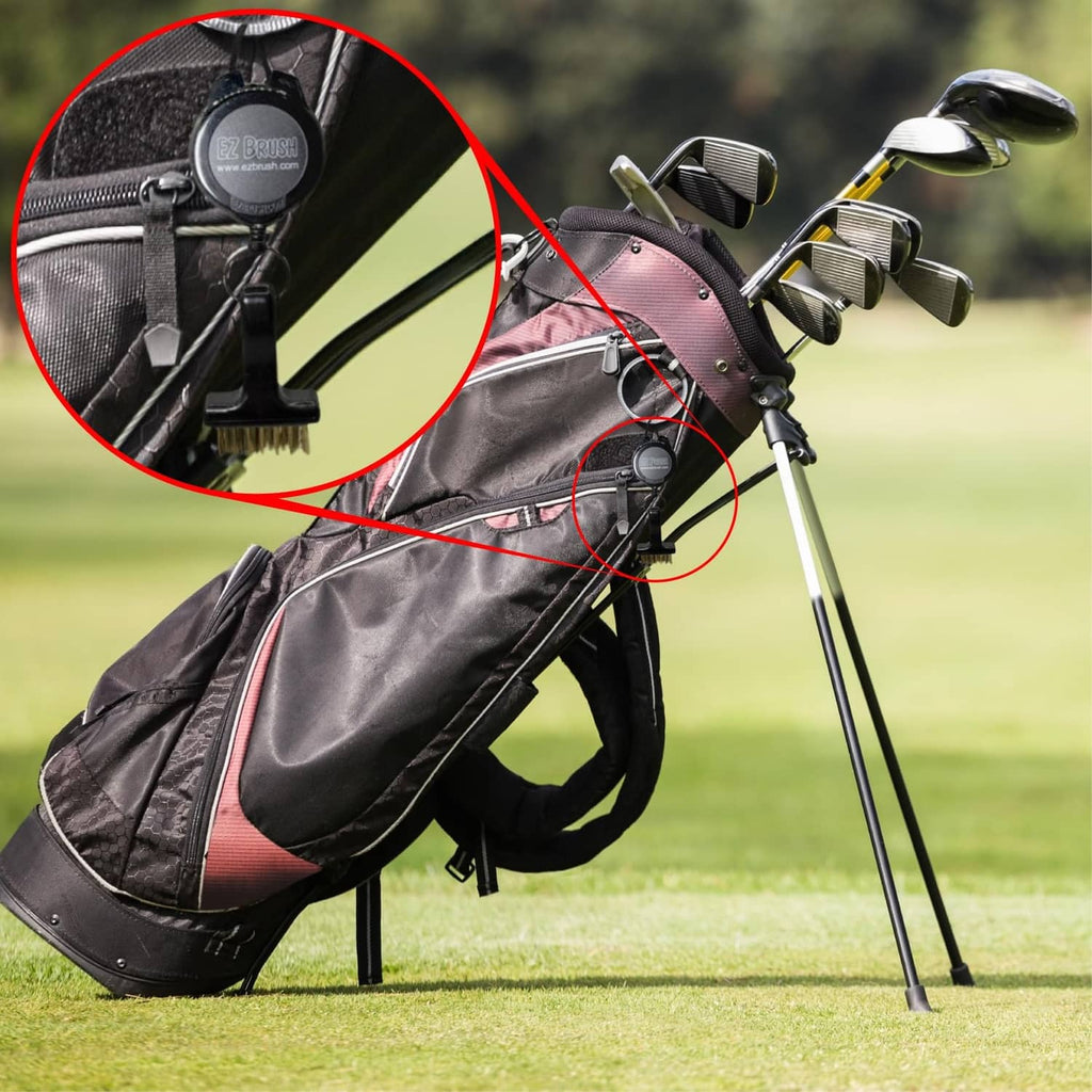 Retractable black EZ BRUSH golf brush tool clipped on bag, gold bristles visible.