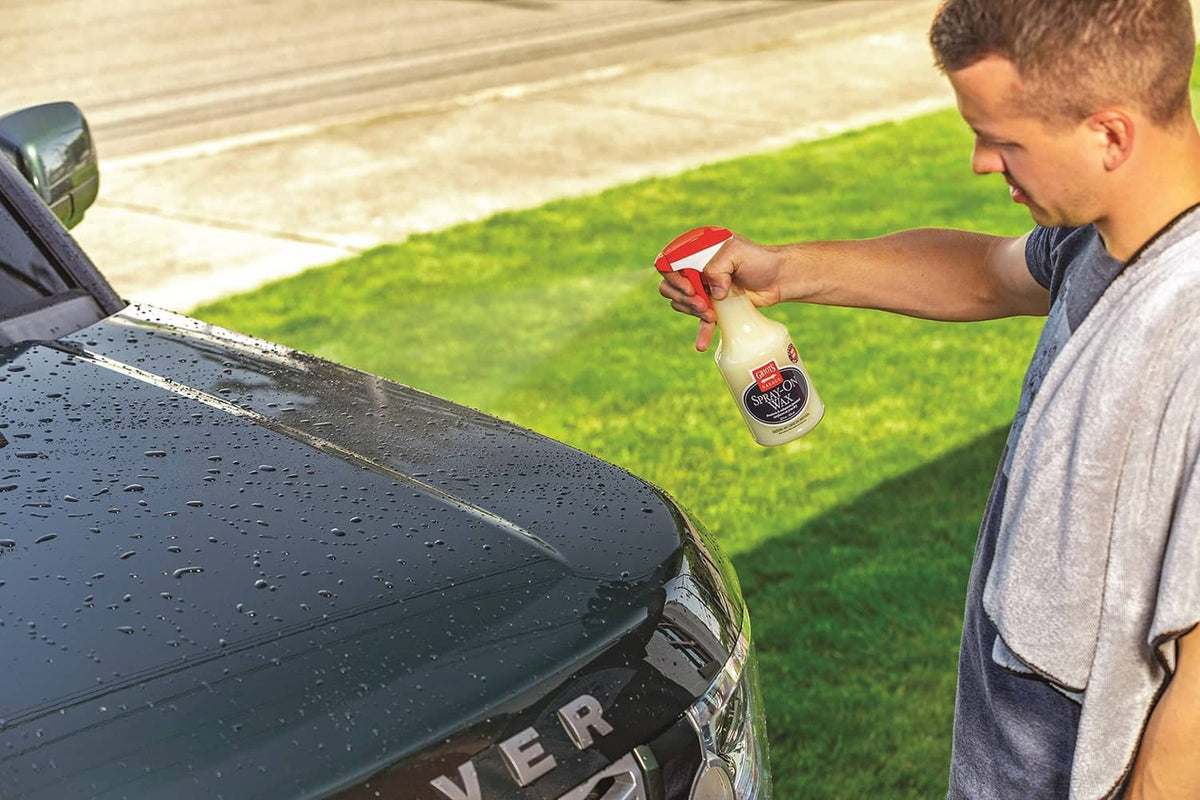 Man spraying spray-on wax onto car hood with a red trigger bottle