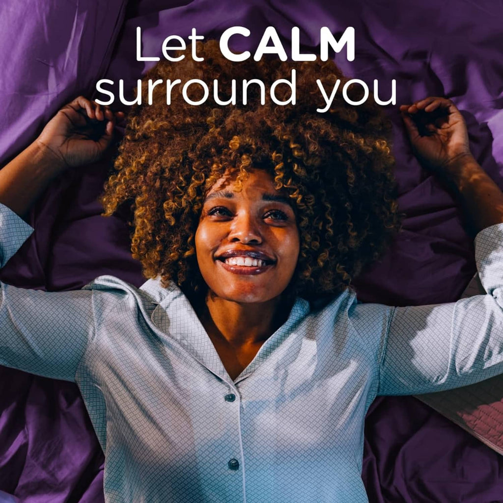 Smiling person relaxing on purple bedding with hands behind head