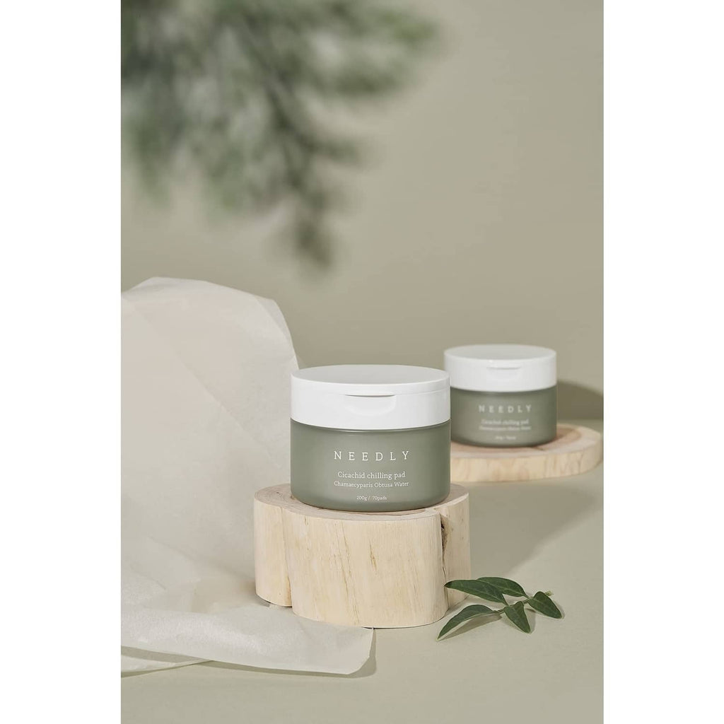 NEEDLY cleansing pad jars with white lids on a round wood stand