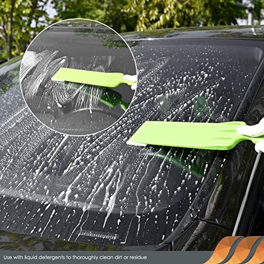 Window tint squeegee scrubbing a car windshield, green rubber blade removing water spots