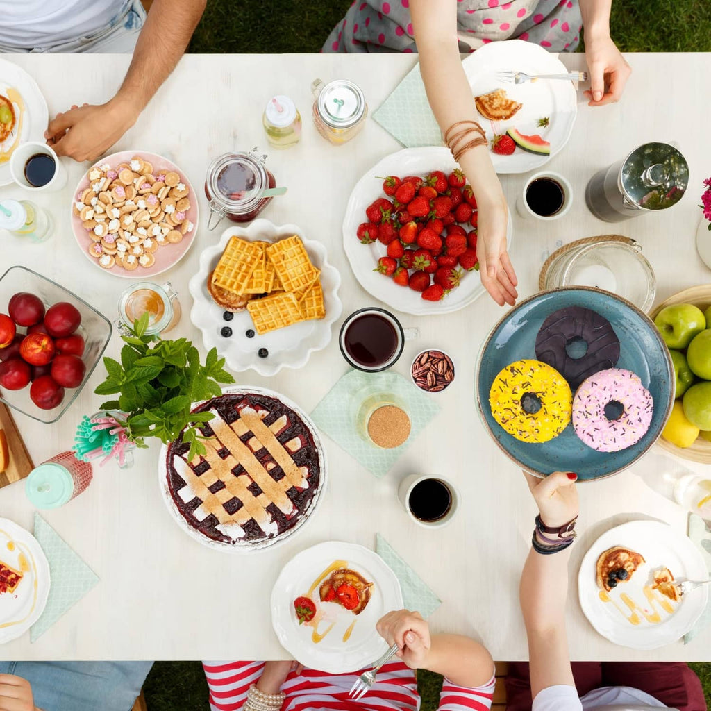 Coffee and dessert party table with mugs, berries, donuts, waffles, and snacks