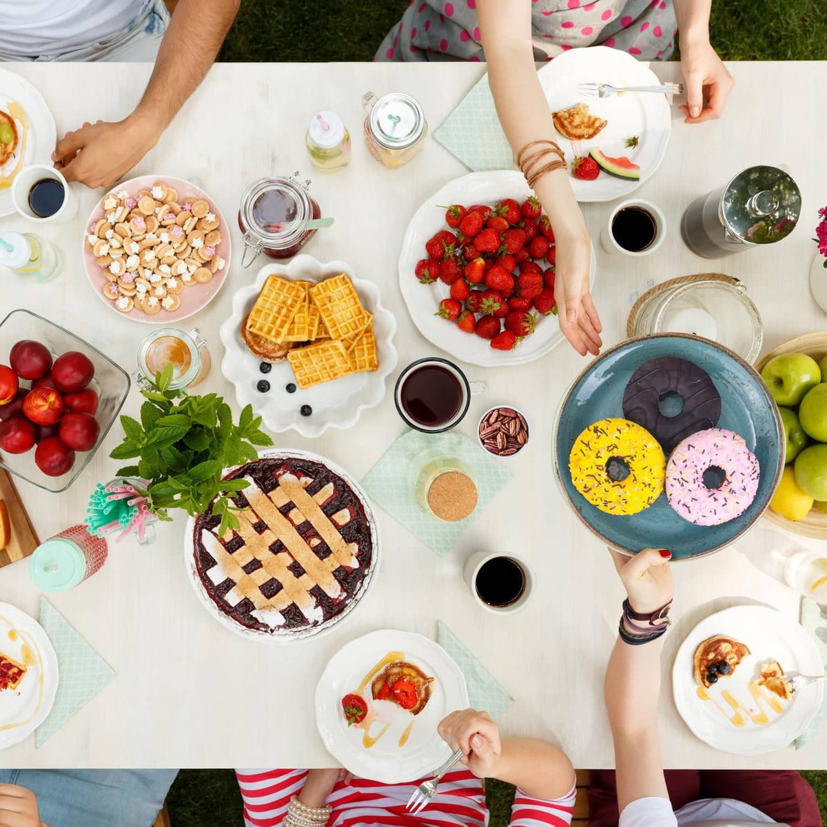 Coffee and dessert party table with mugs, berries, donuts, waffles, and snacks
