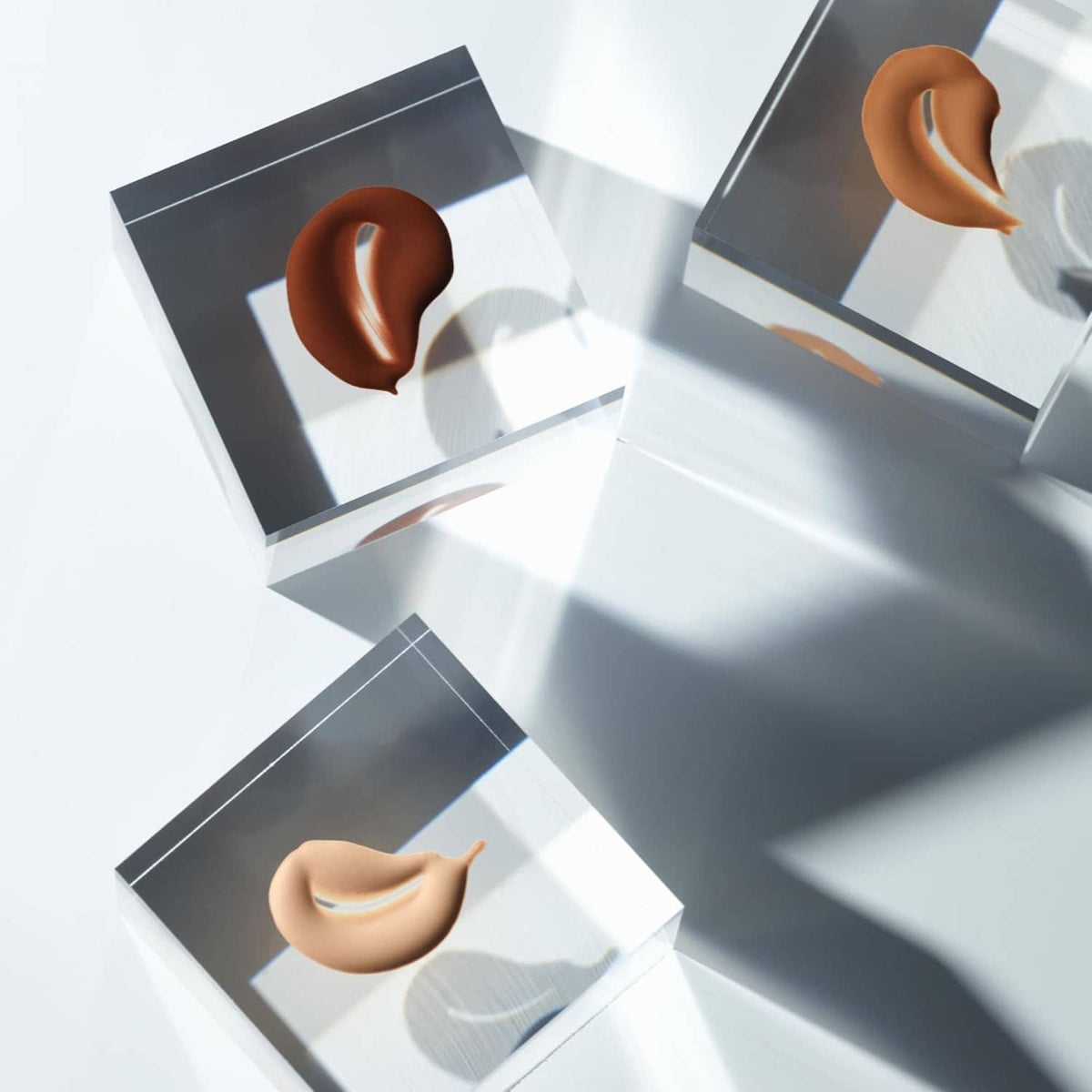 Beige liquid foundation swatches on dark and white sample boxes