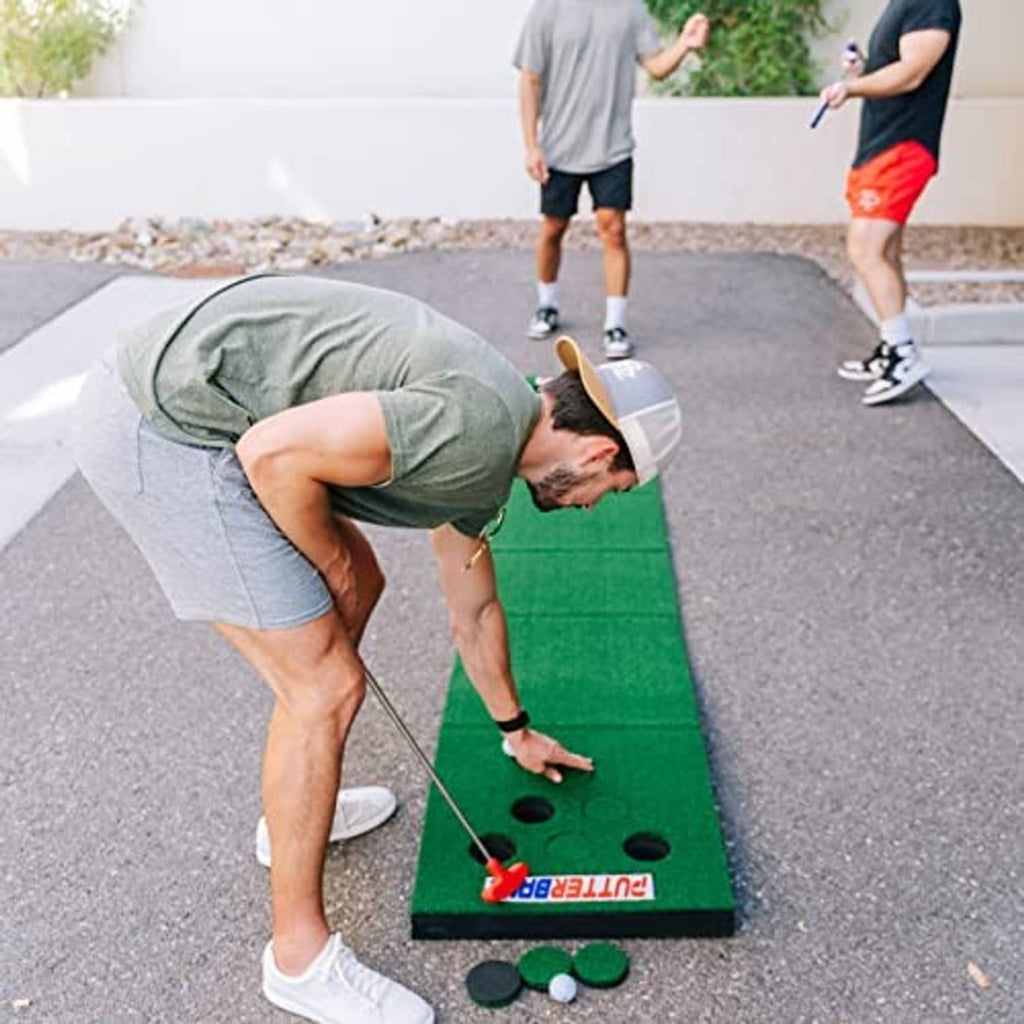 Green turf putting mat with hole cups, red putter, and green/white balls for play.