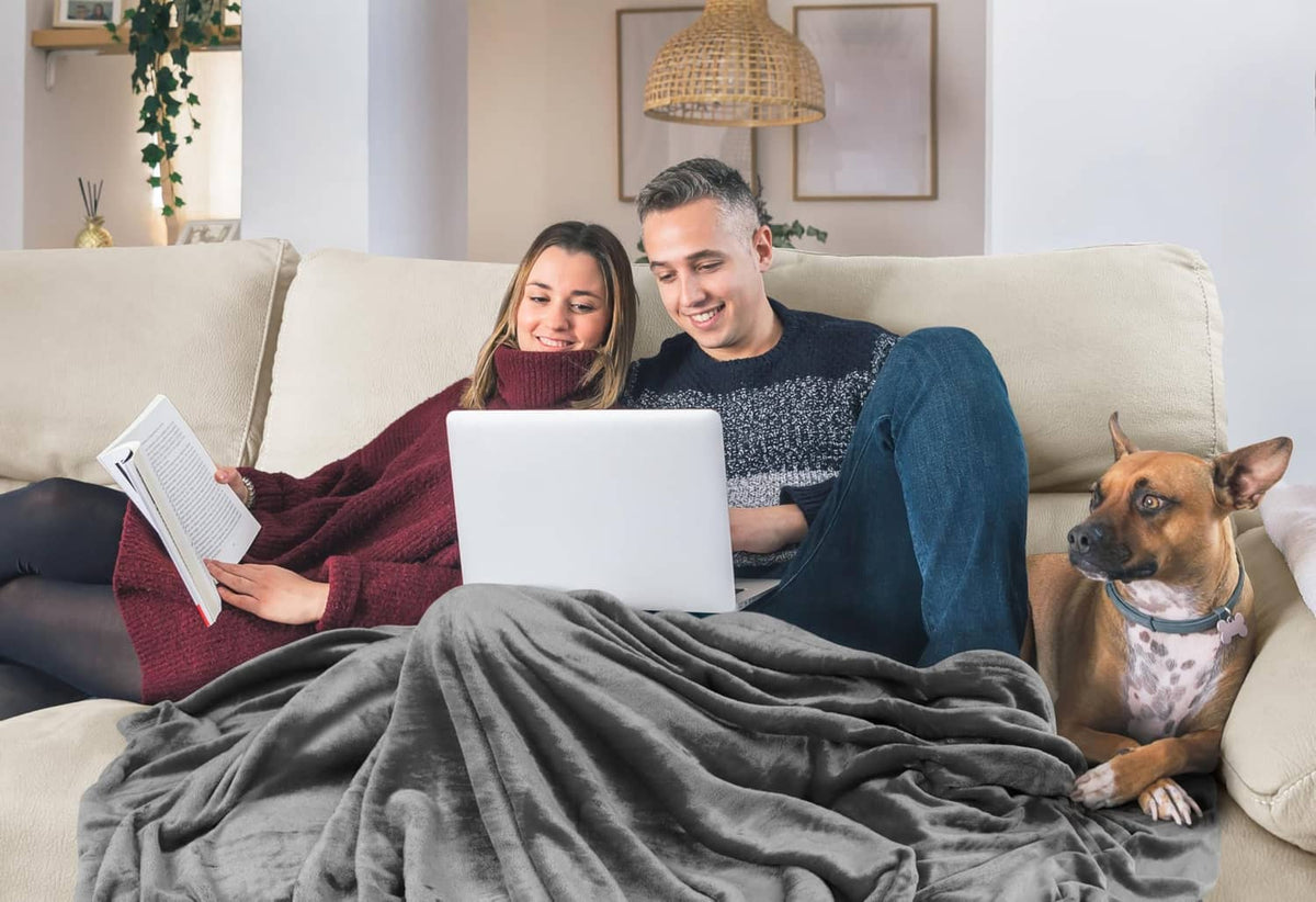 Grey fleece blanket on a living room sofa, wrapped over two people and a dog.