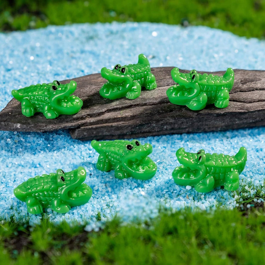 Green mini crocodile resin figurines on blue gravel around a dark rock