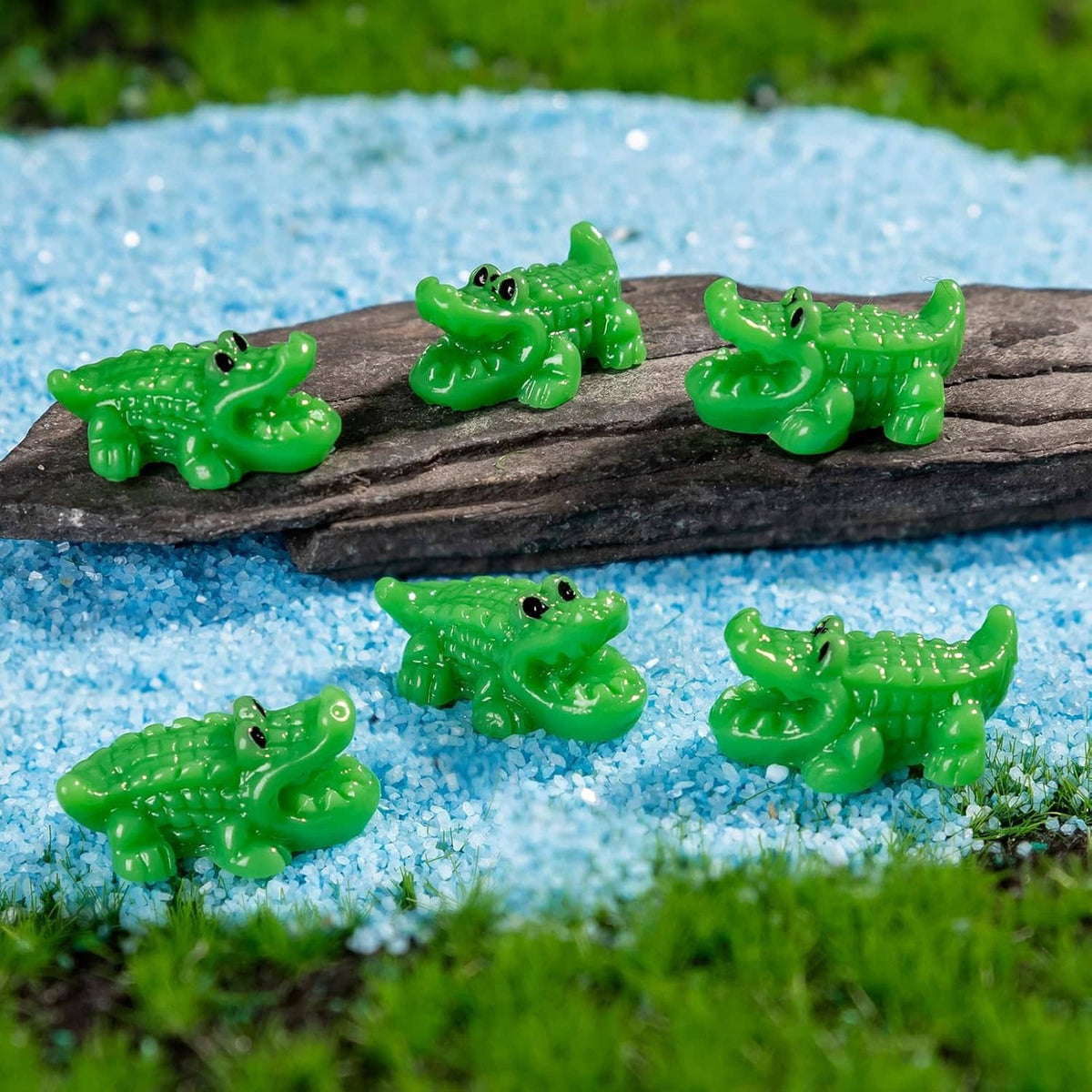 Green mini crocodile resin figurines on blue gravel around a dark rock