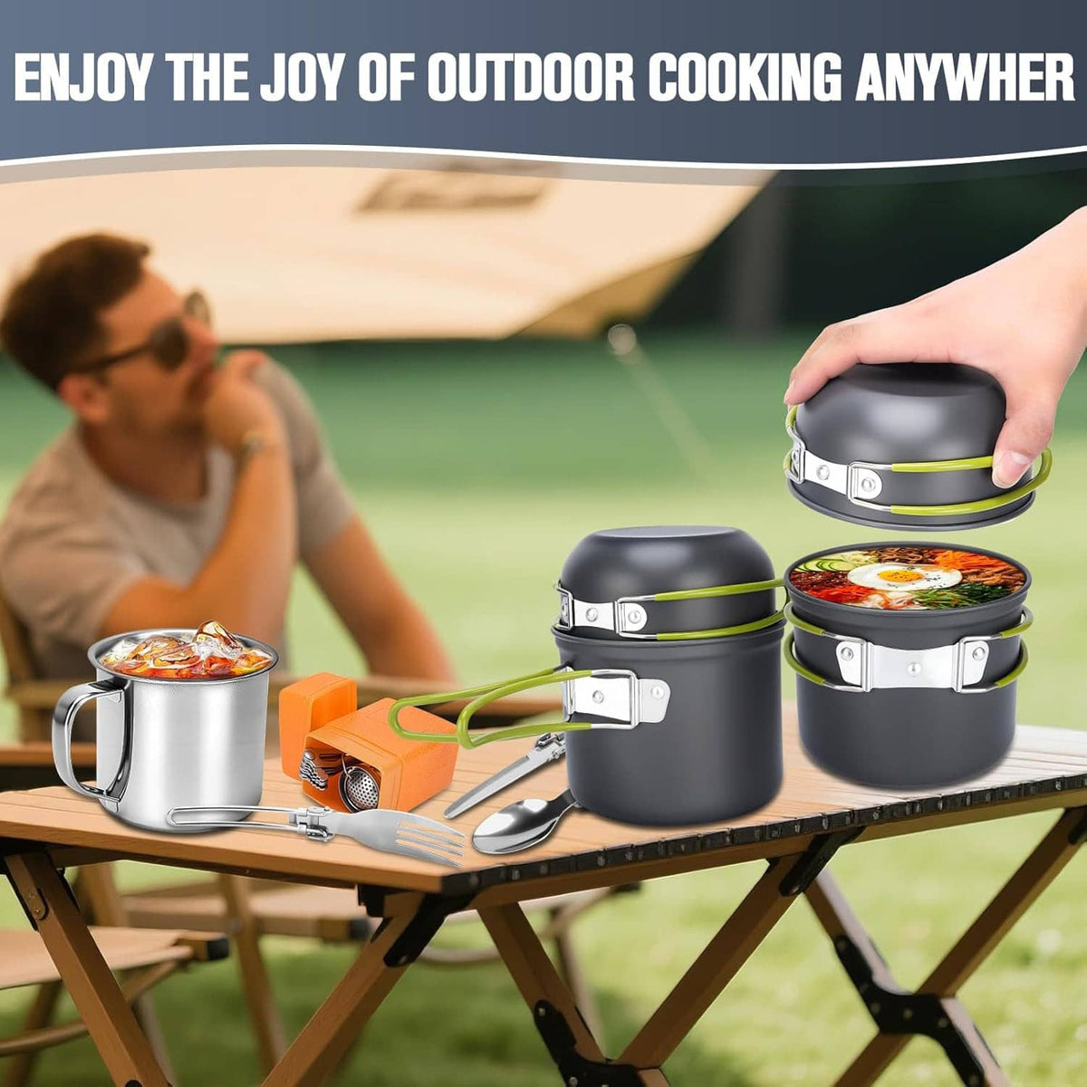 Black stackable camping pots with green-accent handles on tabletop with portable stove