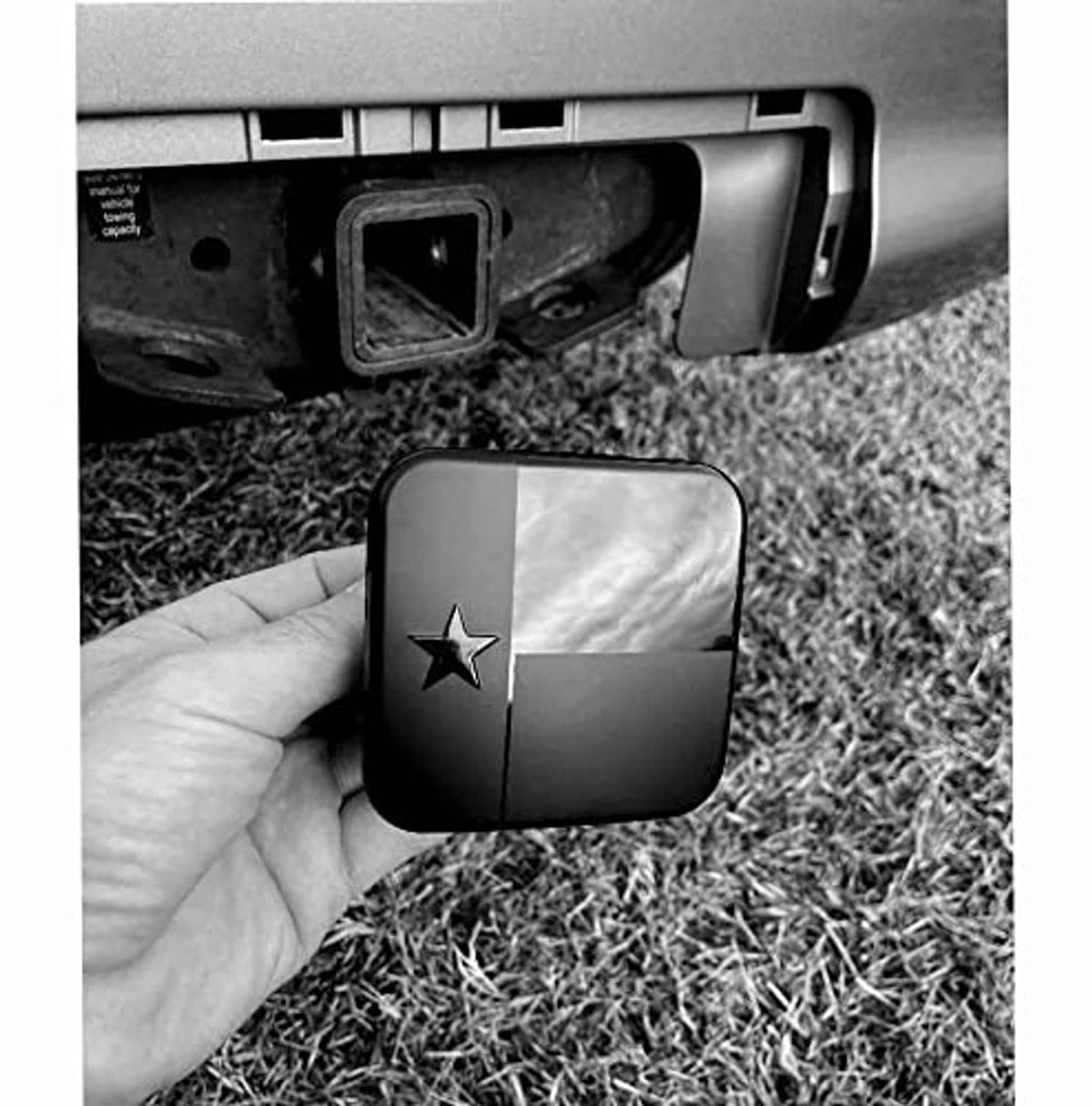 Black hitch receiver cover plug with Texas star emblem, held next to vehicle hitch.