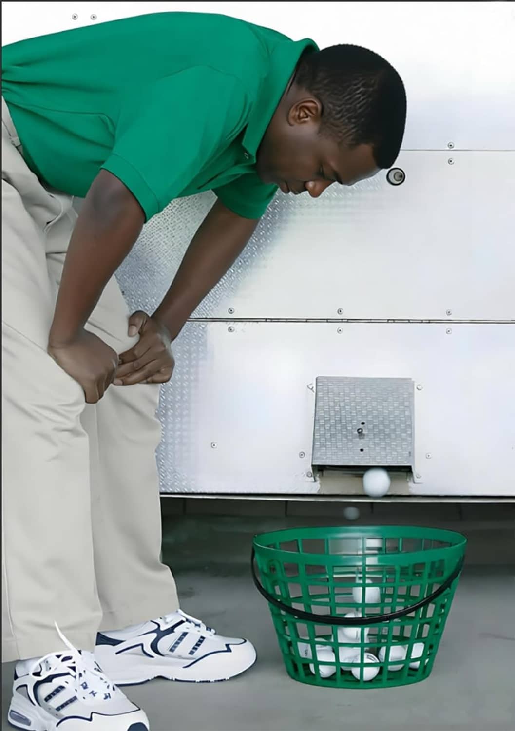 Green golf ball basket with handle sitting on the floor in a storage area