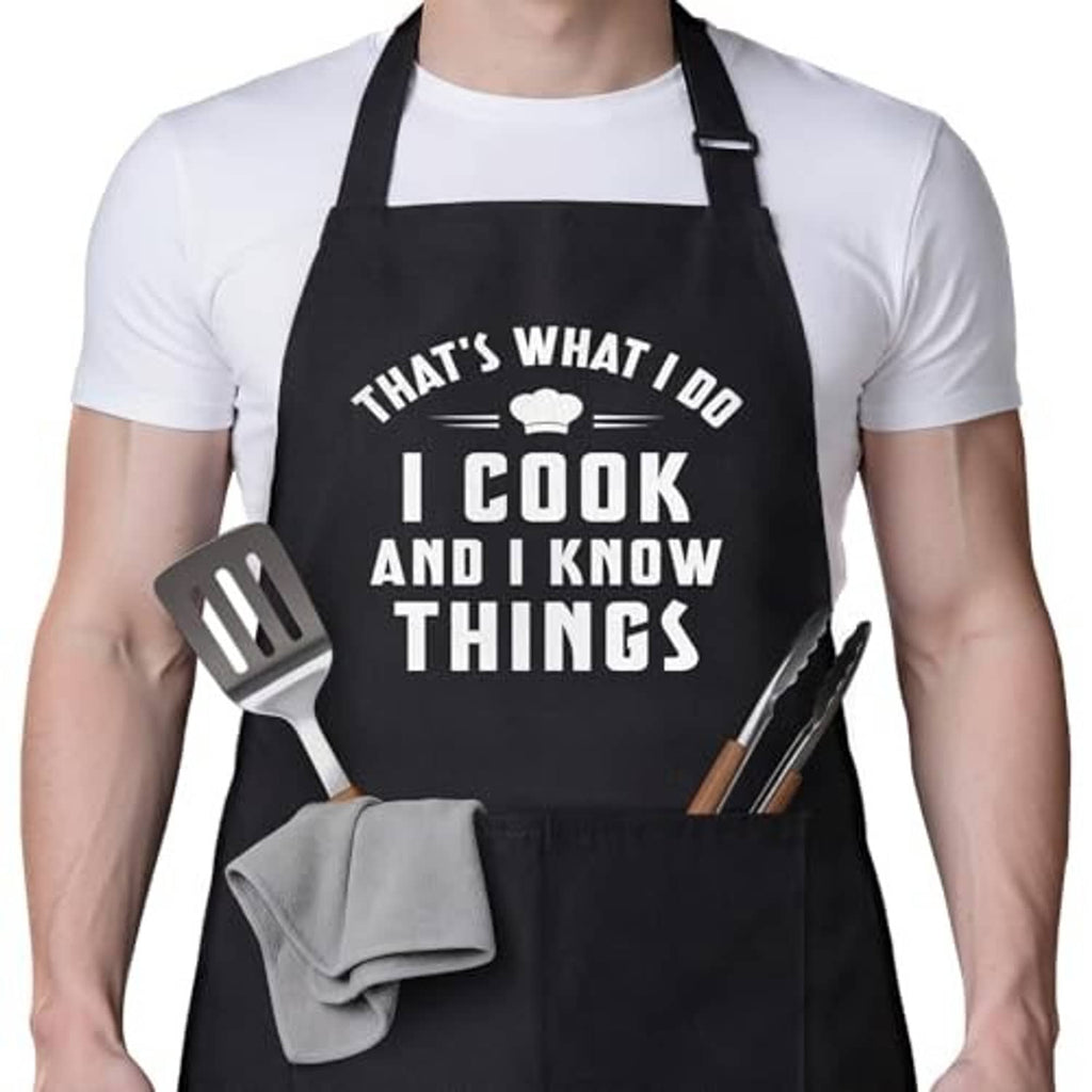 Black cooking apron with centered “I cook and I know things” slogan and front pocket