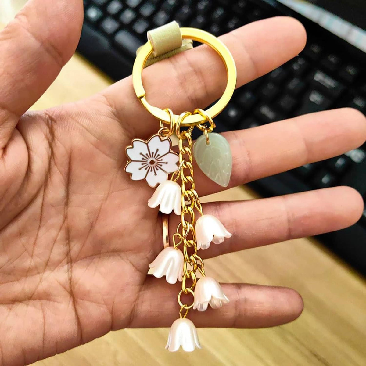 Gold ring leather keychain with white flower and green leaf charms, tassel dangles