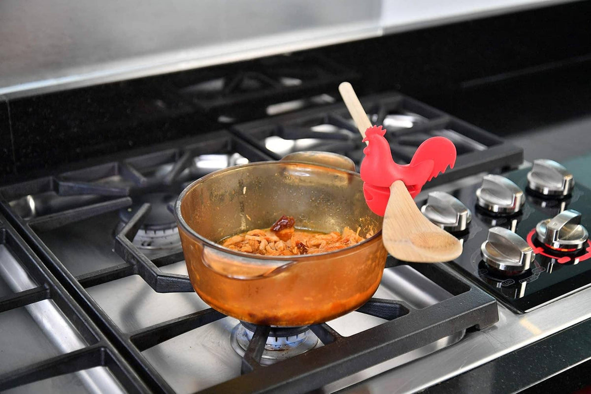 Red rooster spoon holder clipping to skillet on a gas stove