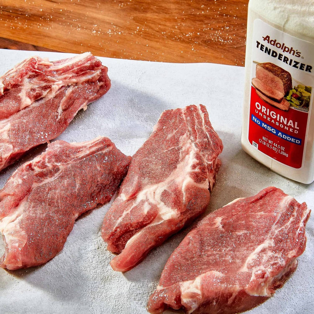 Adolph's Original unseasoned tenderizer bottle with raw meat on parchment