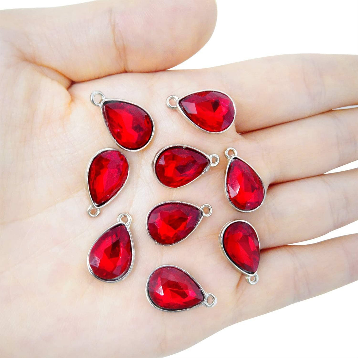 Red teardrop crystal charms with silver-tone loops shown resting on an open palm.