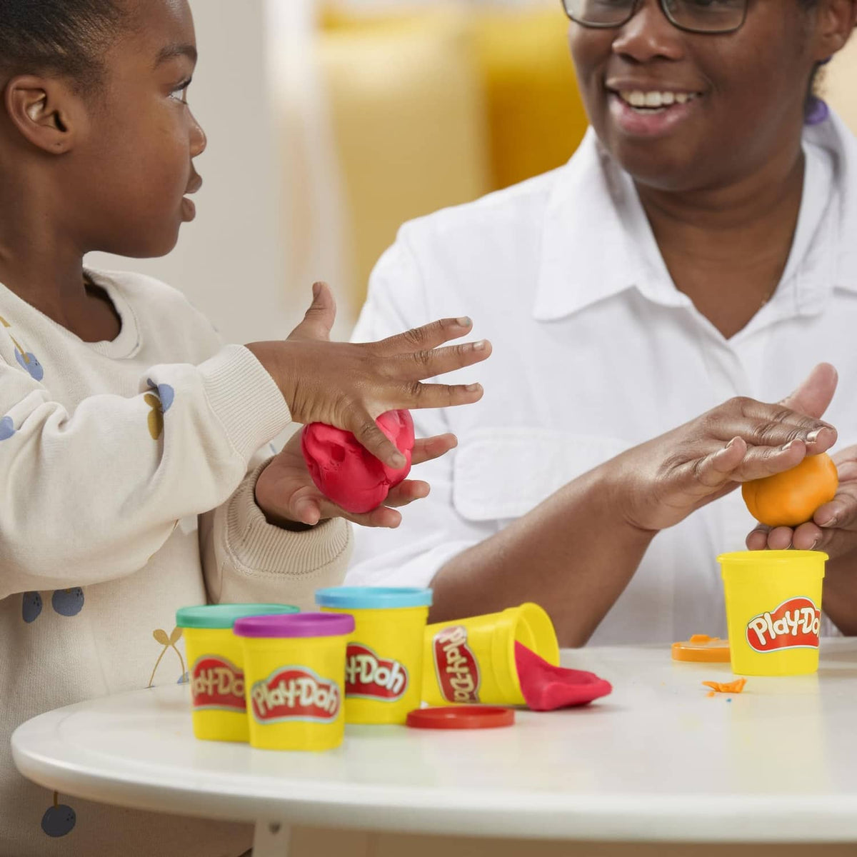 Children play with Play-Doh containers and molded clay pieces on a table