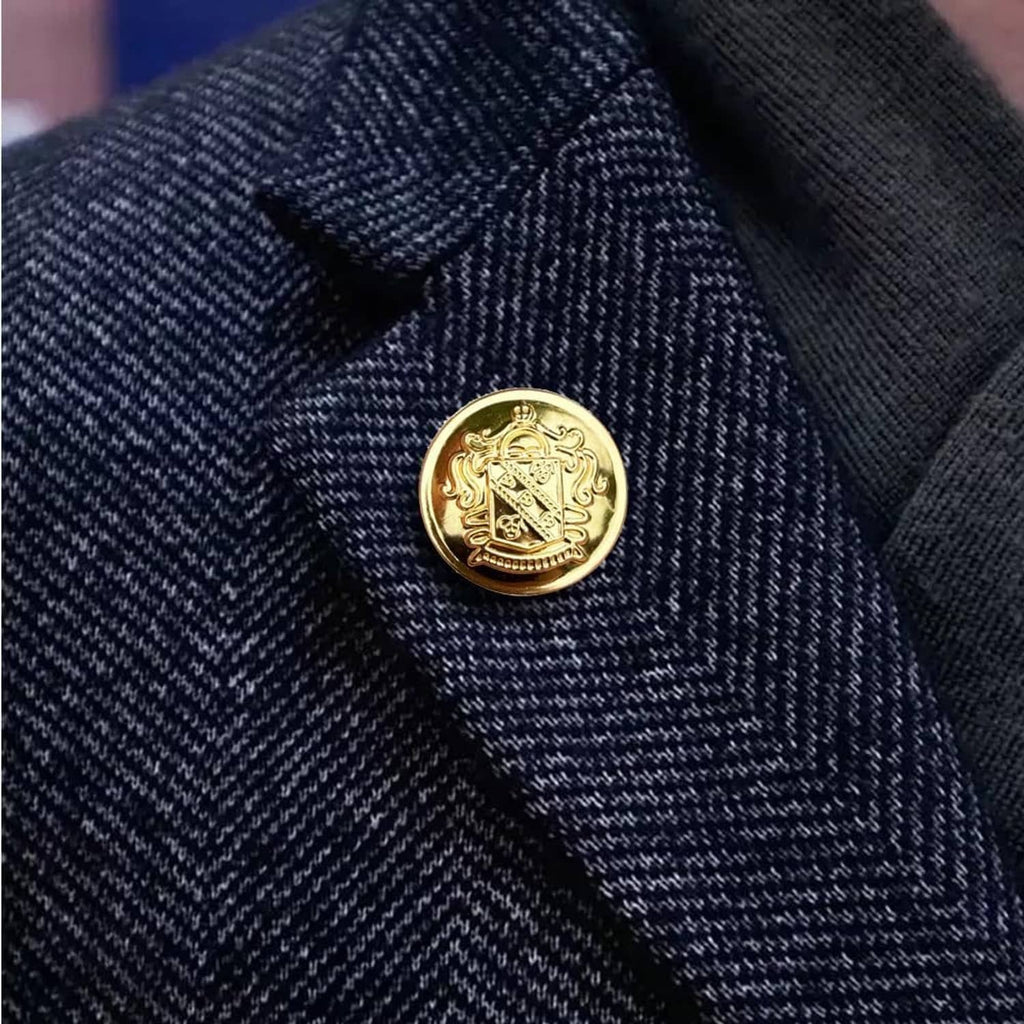 Round gold blazer button with engraved crest, on dark textured fabric