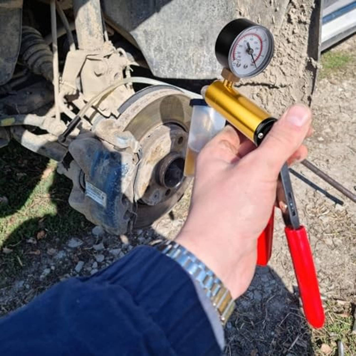 Hand holding gold vacuum pump with pressure gauge attached to car brake component