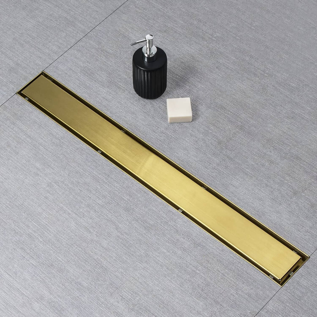 Gold linear shower drain grate with mounting stem, black threaded adapter, and leveling foot