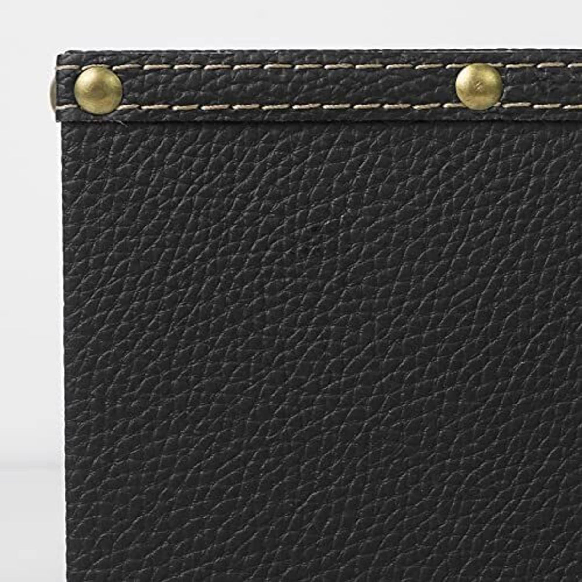 Black leather remote holder detail with textured surface, stitched edge, and brass stud