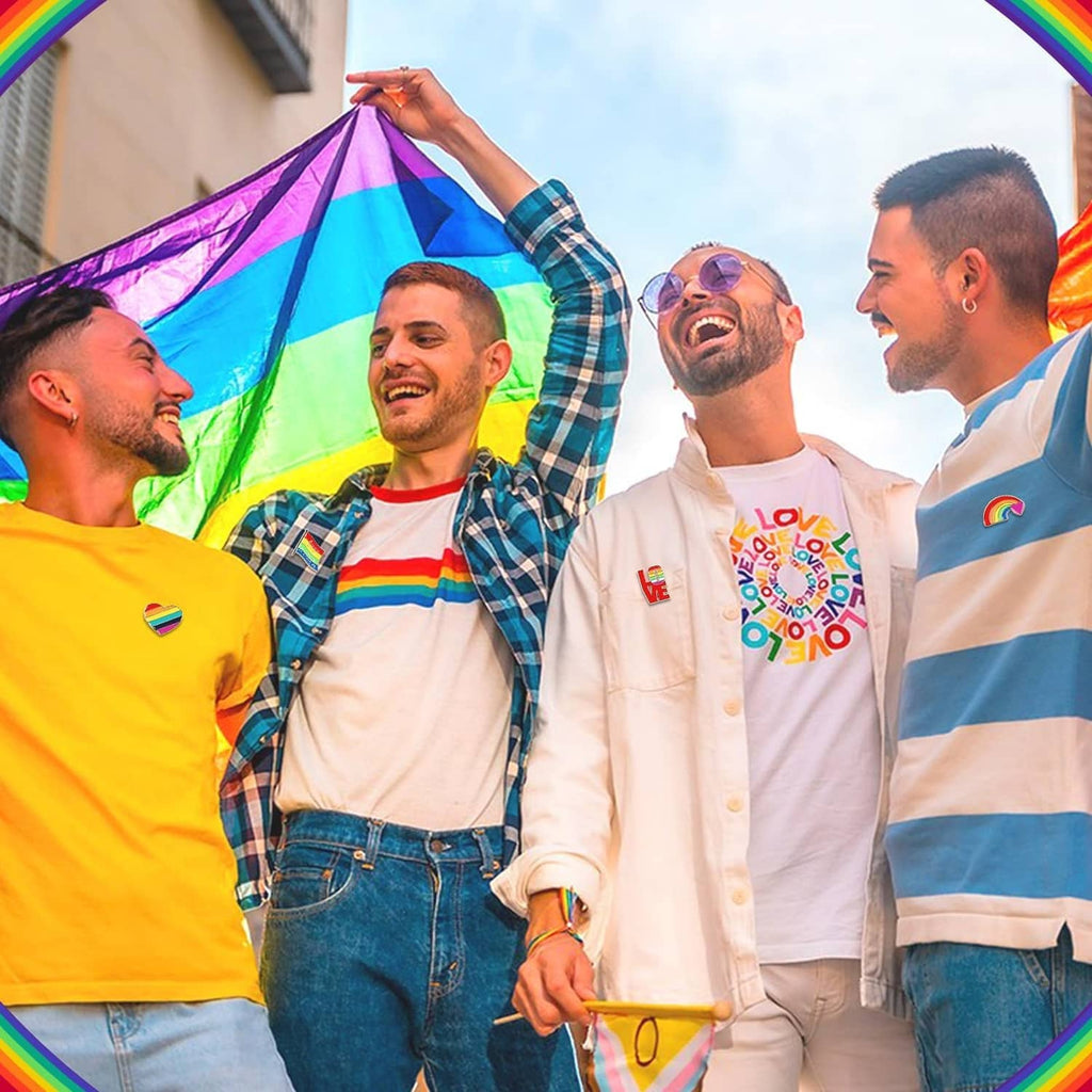 Rainbow Pride enamel pins on shirts of people standing outdoors with a rainbow flag.
