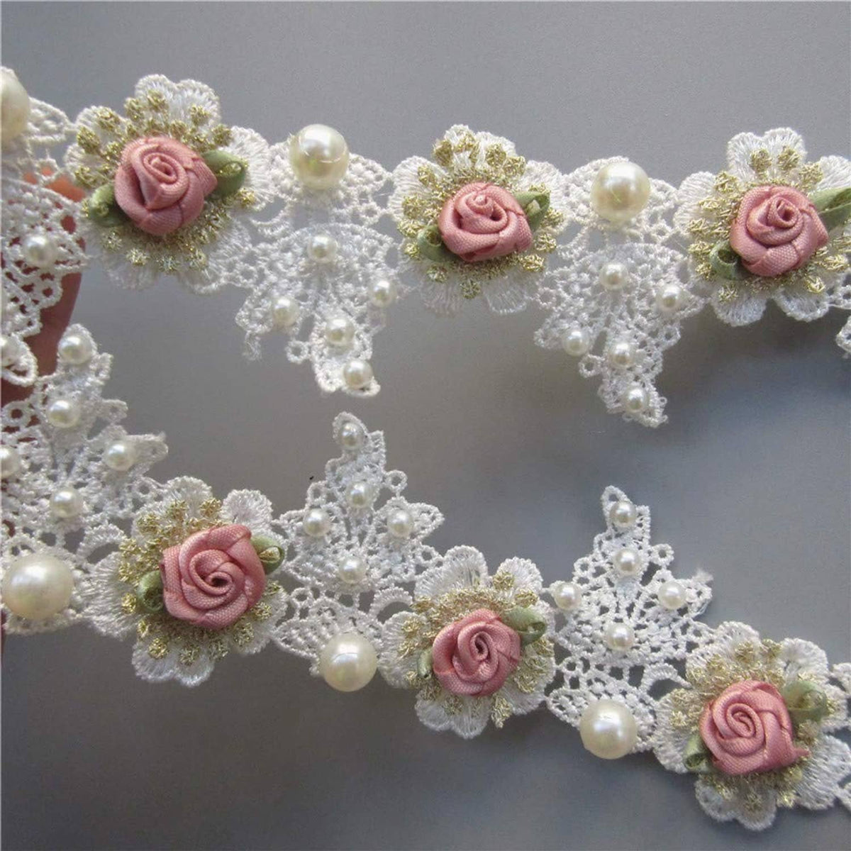 Close-up white lace trim with pink rose blooms and scattered pearl bead accents