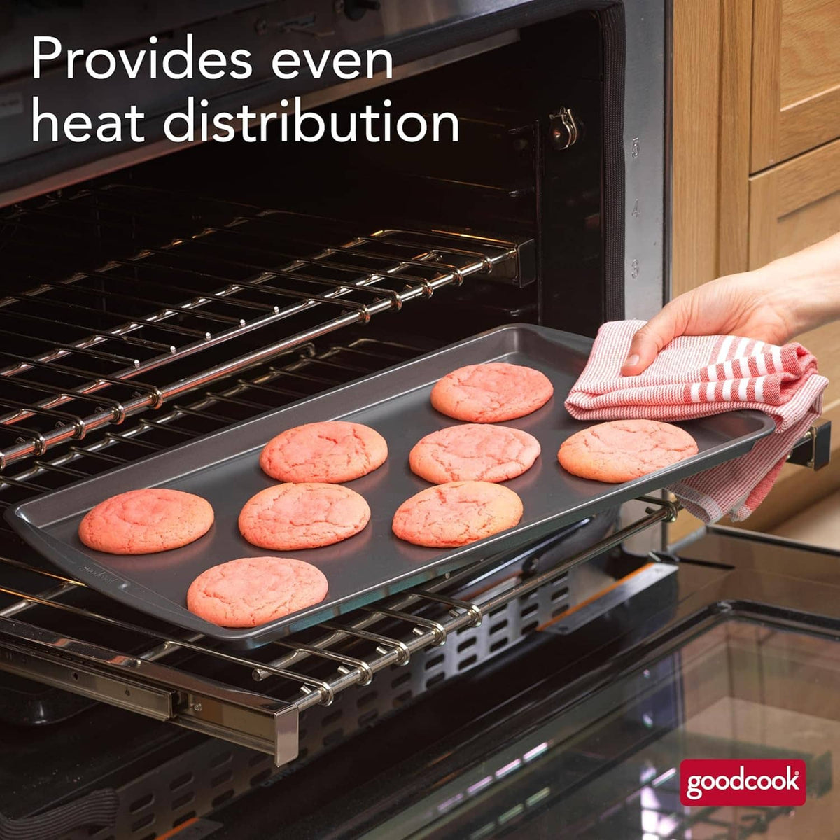 Gray nonstick baking sheet in oven, with pink cookies and hand placing one