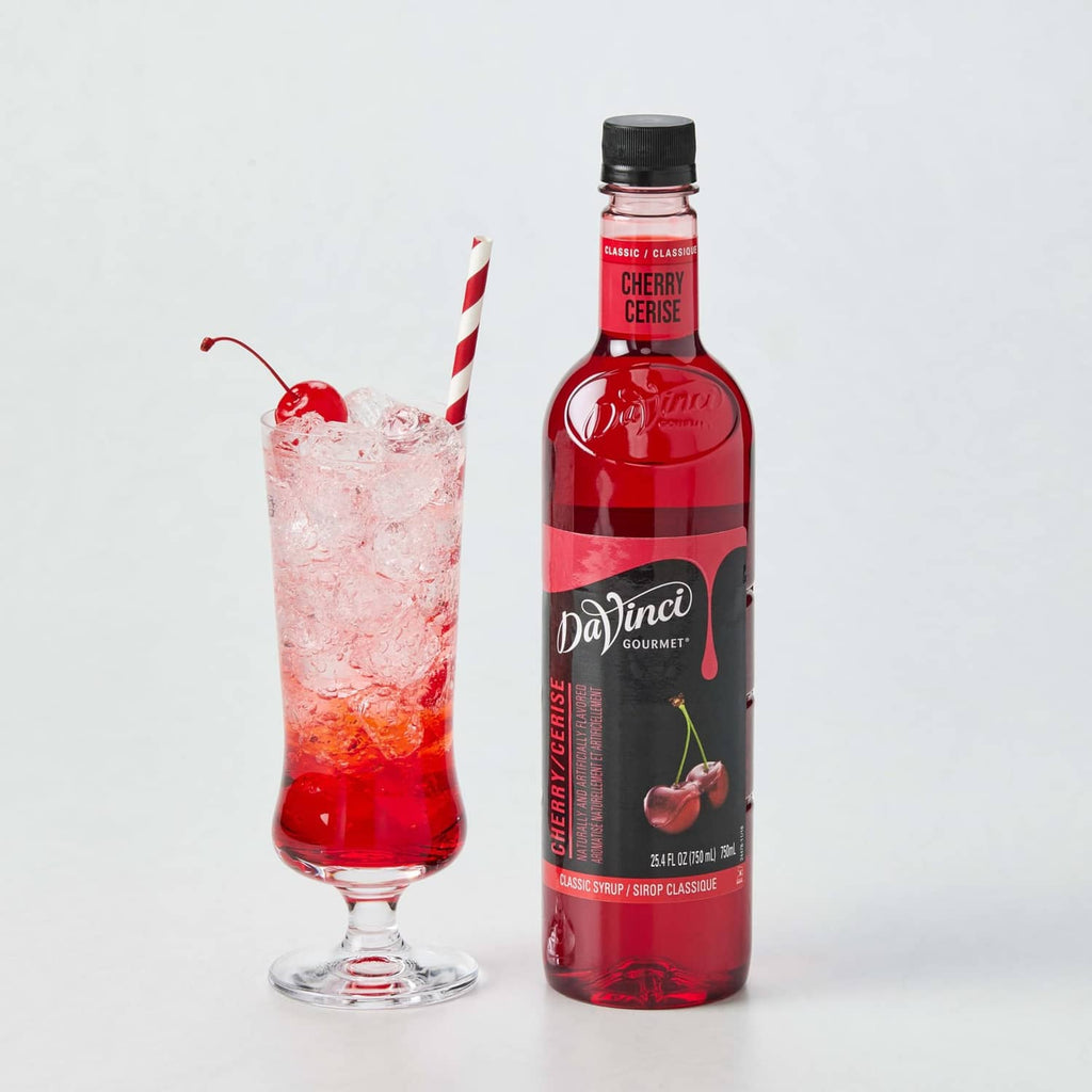 Cherry syrup bottle with red liquid beside a glass drink with ice
