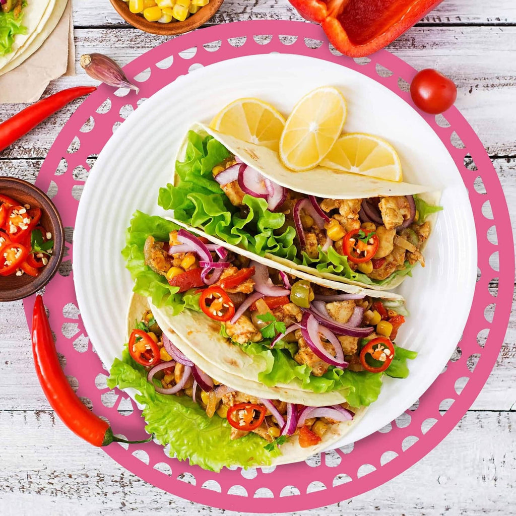 Pink circular paper place mat with cutout decorative border under a taco platter