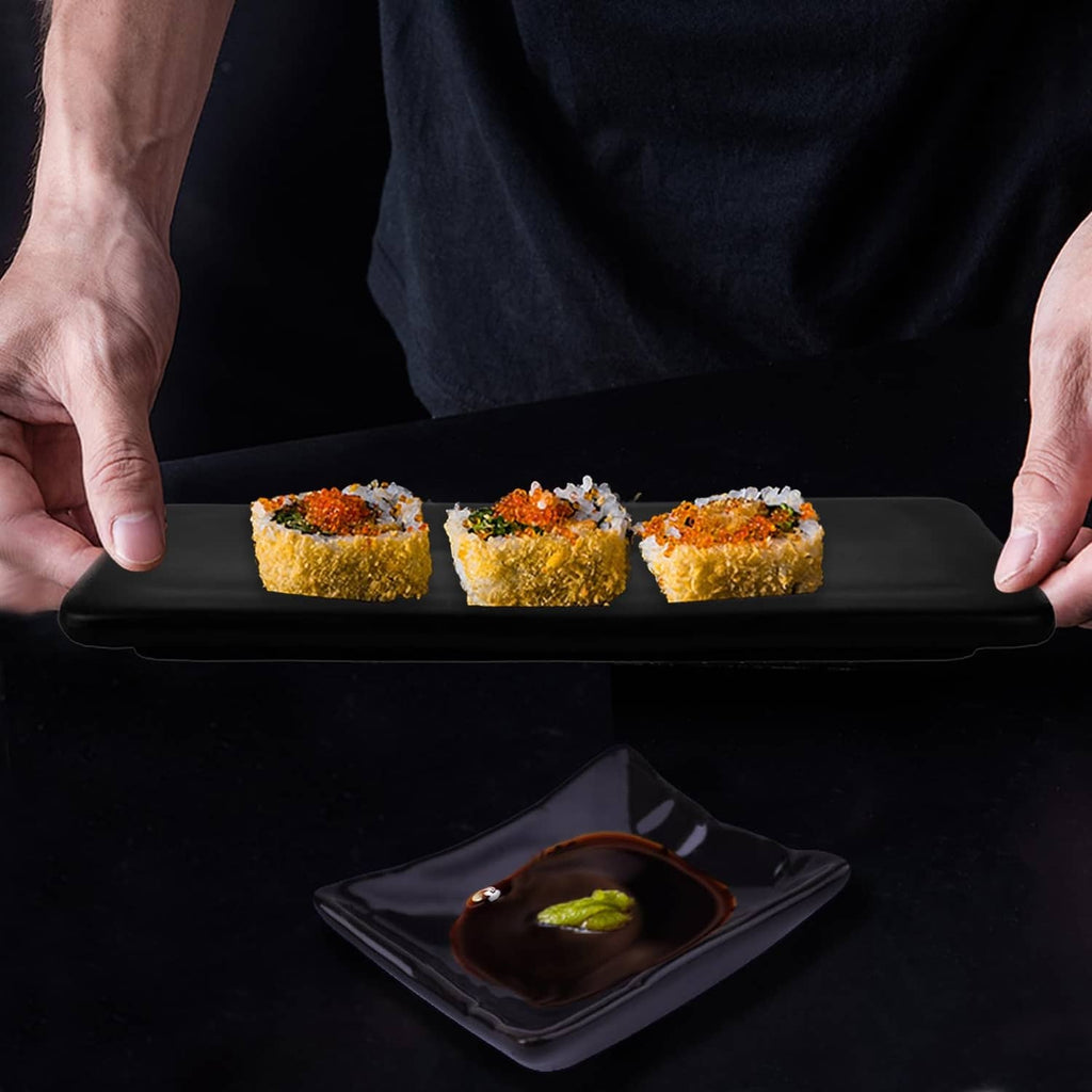 Black sushi plate held in hands with three rolls and small square soy dish