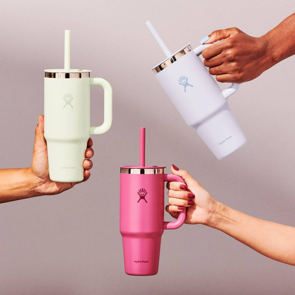 Travel tumblers with handles and straws in light green and white, held by hands.
