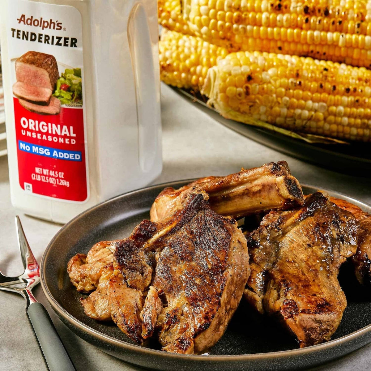 Adolph's tenderizer bottle beside grilled pork chops on a dark plate