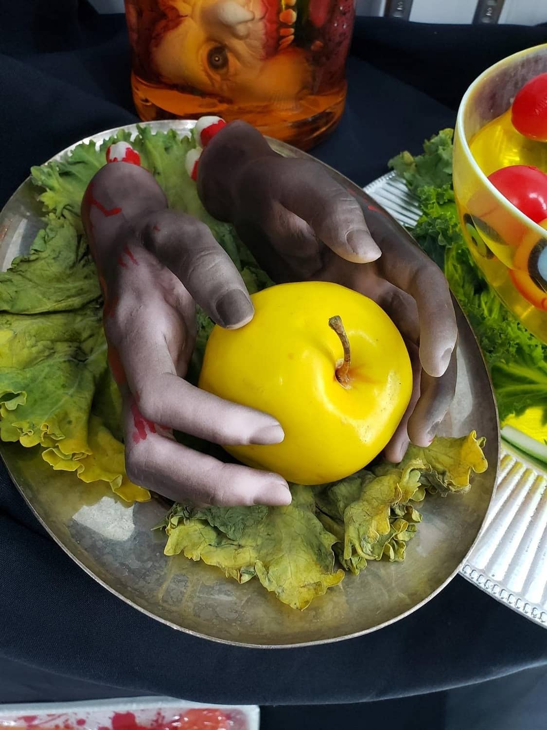 Halloween severed hand props with red blood stains resting on a table with carved pumpkin