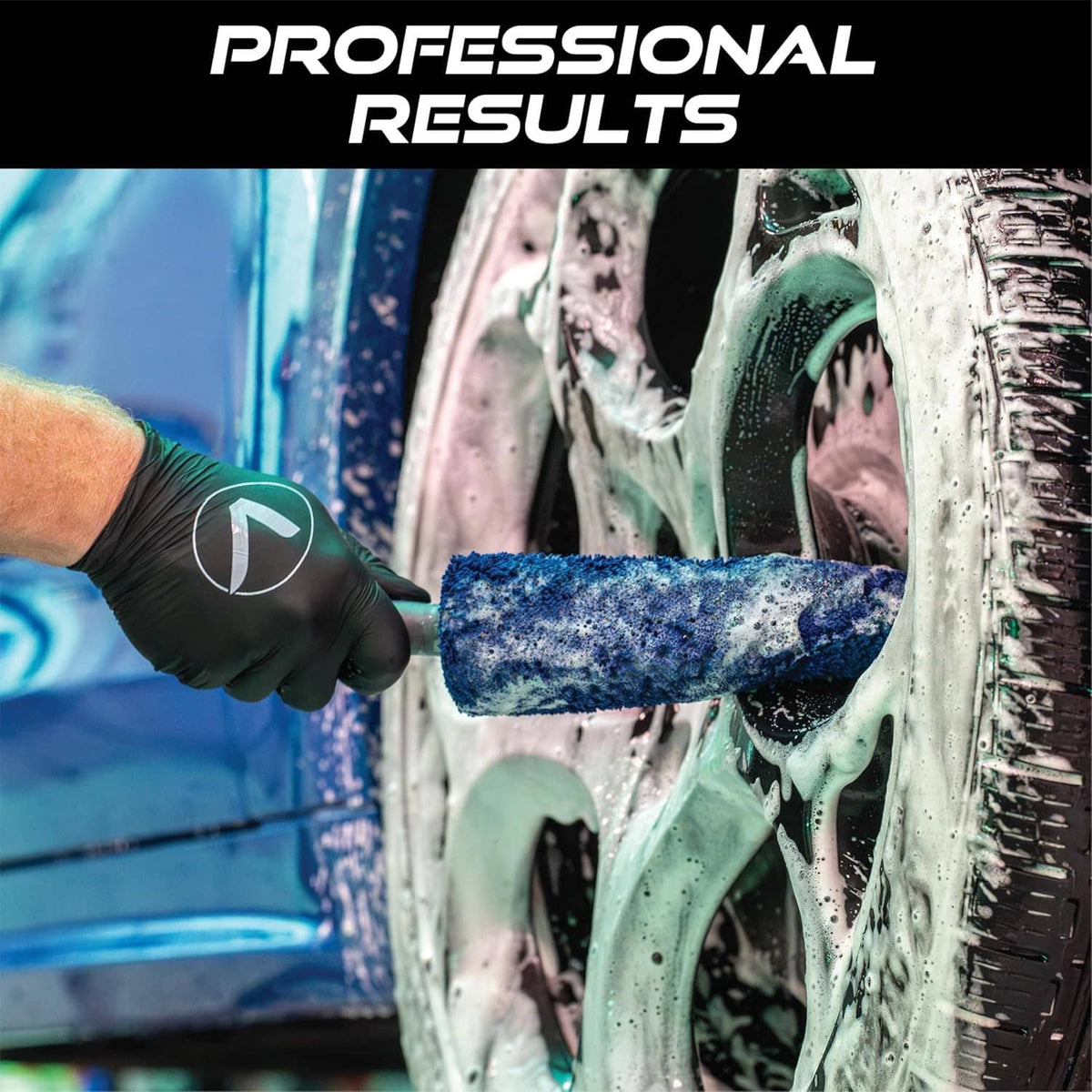 Gloved hand using a blue microfiber wheel brush on a car rim with cleaner foam