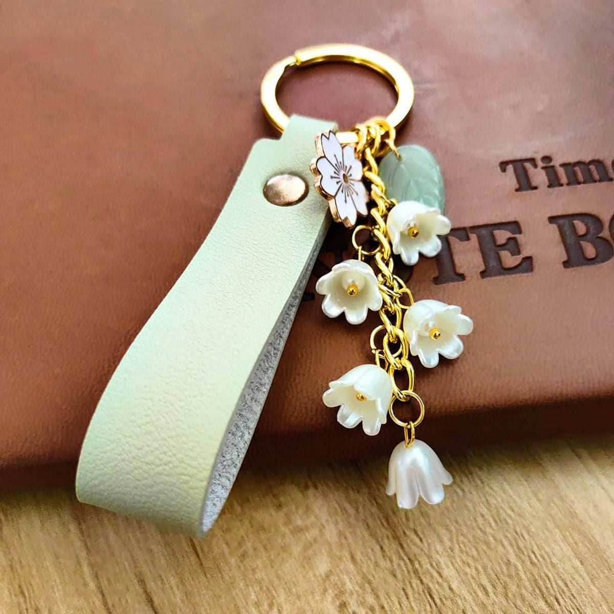 Mint green leather keychain with gold ring, white lily flower charm, and tassel dangles