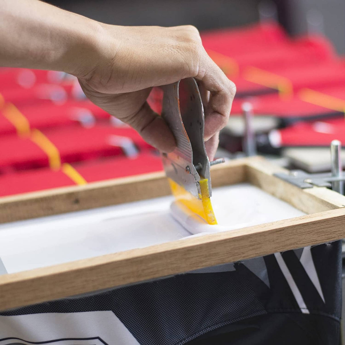 Wood screen printing frame with mesh in use; hand squeegee across print area