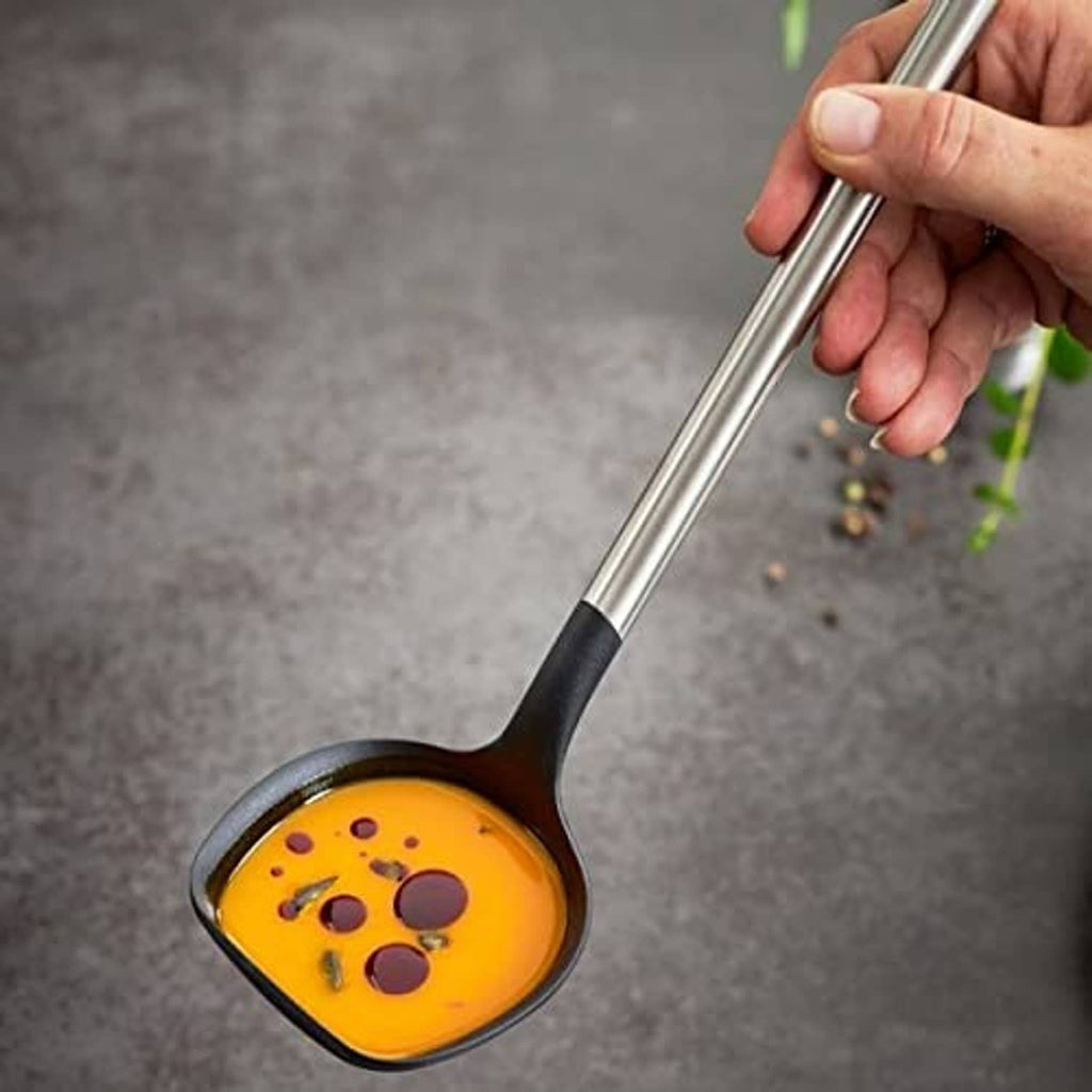 Black-and-silver soup ladle lifting orange soup with visible pepper topping