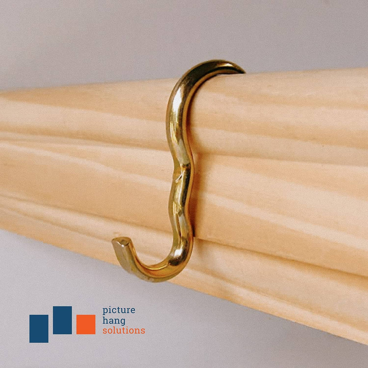 Brass-finish narrow picture rail hook mounted on a light wood rail