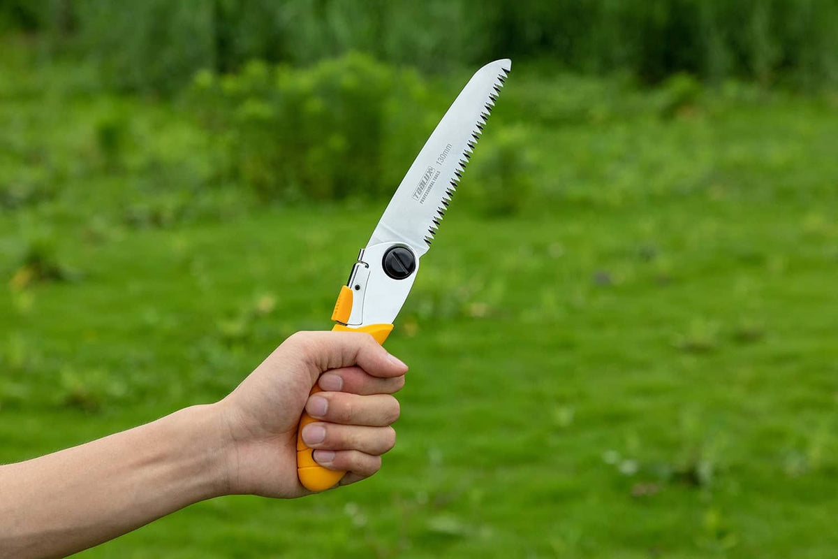 Folding pruning hand saw held in hand, yellow handle with extended silver blade