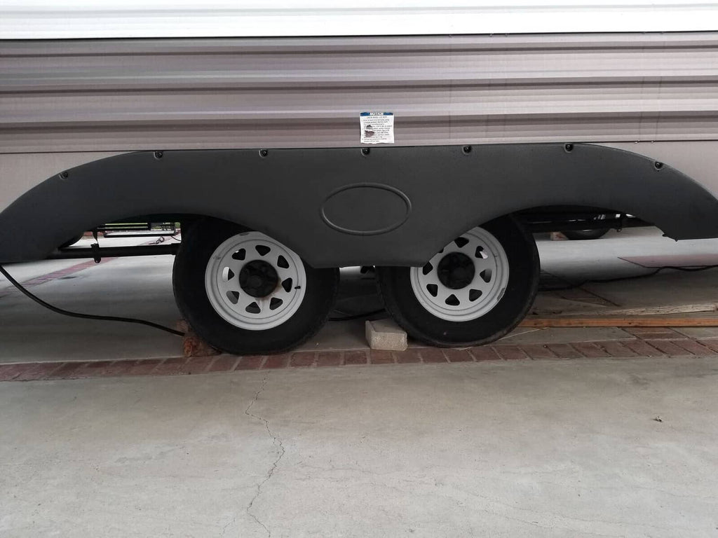 Black trailer fender skirt installed over wheel wells, curved molded cover with oval center