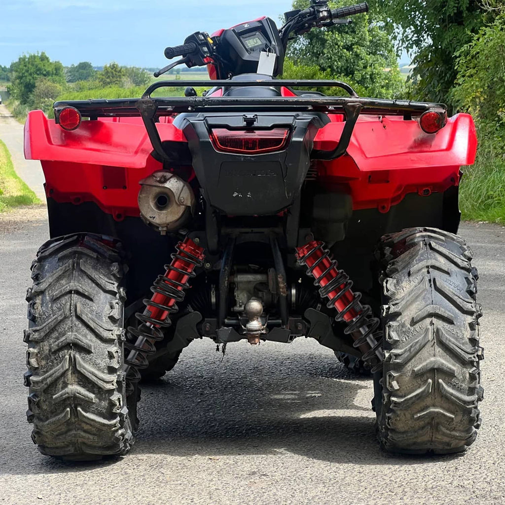 ATV rear suspension featuring two red adjustable shock absorbers with black coil springs